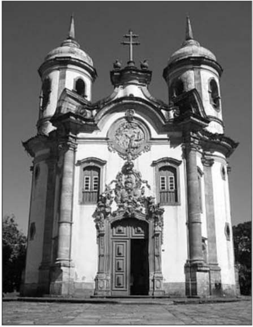 Fotografia em preto e branco da fachada da igreja de São Francisco de Assis, em Ouro Preto, em estilo barroco/rococó mineiro, com torres cilíndricas e frontispício esculpido.