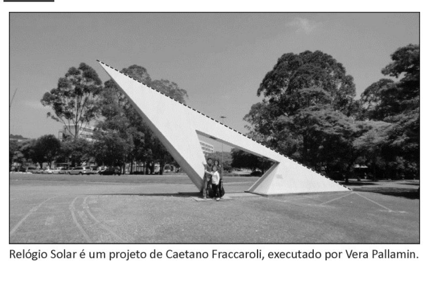 Fotografia de um grande monumento triangular branco, o Relógio Solar, com uma linha reta tracejada ao longo da sua aresta superior inclinada. Na base, pessoas posam para escala. Abaixo da foto consta a legenda: "Relógio Solar é um projeto de Caetano Fraccaroli, executado por Vera Pallamin."