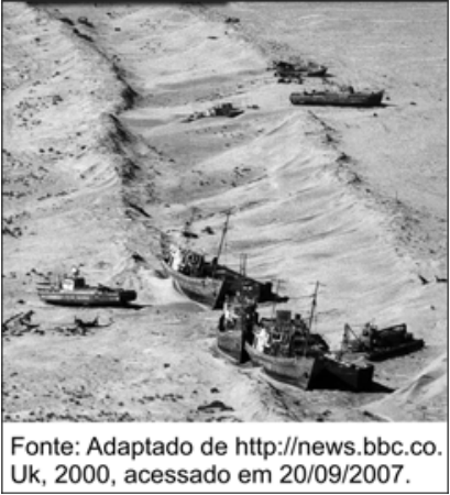 Fotografia em preto e branco mostrando embarcações pesqueiras abandonadas e encalhadas sobre a areia do leito seco do mar de Aral. Na parte inferior consta: Fonte: Adaptado de http://news.bbc.co.Uk, 2000, acessado em 20/09/2007.