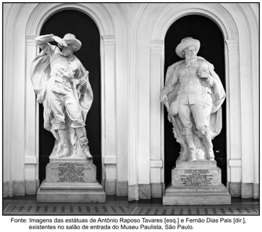 Fotografia em preto e branco exibindo duas estátuas de mármore posicionadas em nichos com arcos plenos no salão de entrada do Museu Paulista. À esquerda, a estátua de Antônio Raposo Tavares em pose dinâmica, com uma das mãos sobre os olhos observando o horizonte, vestindo gibão, chapéu e botas de cano alto. À direita, a estátua de Fernão Dias Pais, retratado com barba longa, chapéu, capa e botas, segurando um cajado. Ambas as esculturas repousam sobre pedestais com inscrições comemorativas. Abaixo da imagem lê-se: Fonte: Imagens das estátuas de Antônio Raposo Tavares [esq.] e Fernão Dias Pais [dir.], existentes no salão de entrada do Museu Paulista, São Paulo.