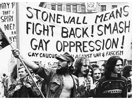 Fotografia em preto e branco de pessoas marchando em um protesto segurando uma faixa com os dizeres: "STONEWALL MEANS FIGHT BACK! SMASH GAY OPPRESSION! GAY CAUCUS - YOUTH AGAINST WAR & FASCISM".