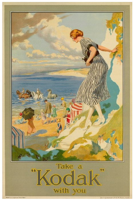 F2 Propaganda da Kodak com a ilustração de uma mulher de vestido listrado descendo uma encosta rochosa em direção a uma praia, segurando uma câmera fotográfica. Na praia ao fundo, veem-se banhistas, barracas e pessoas a cavalo na água. Na base da imagem, lê-se: “Take a ‘Kodak’ with you”.