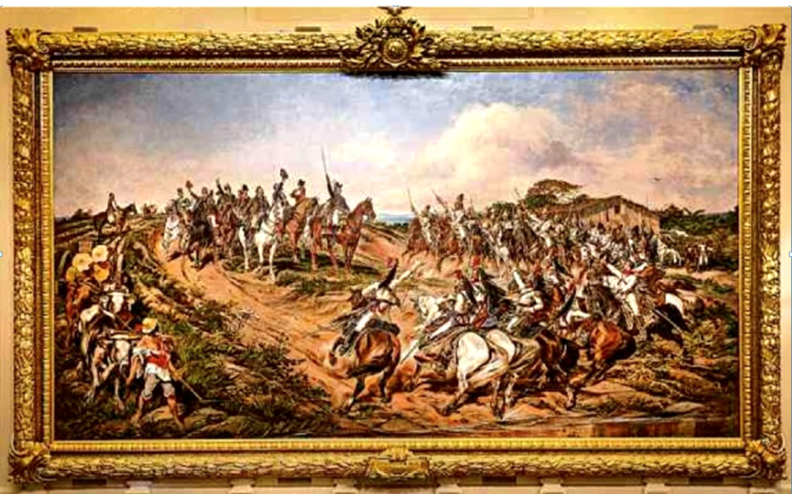 Reprodução do quadro Independência ou Morte, em moldura dourada ornamentada. Em uma paisagem rural, um grupo de cavaleiros está no alto de uma elevação, ao centro e à esquerda, diante de uma formação de soldados montados a cavalo que ocupa o lado direito e o primeiro plano. Vários homens erguem espadas. À esquerda, há um homem junto a bois e a um carro carregado. Ao fundo, aparecem vegetação, uma construção e céu com nuvens.