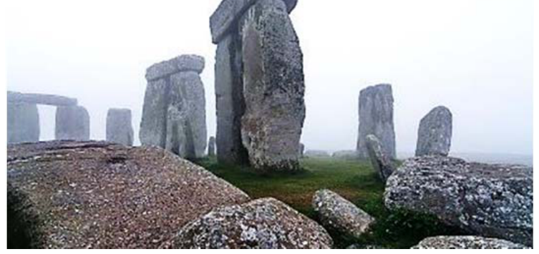 Fotografia do monumento megalítico de Stonehenge em meio à névoa, exibindo grandes blocos de pedra dispostos em círculos concêntricos com pedras na vertical sustentando blocos horizontais.