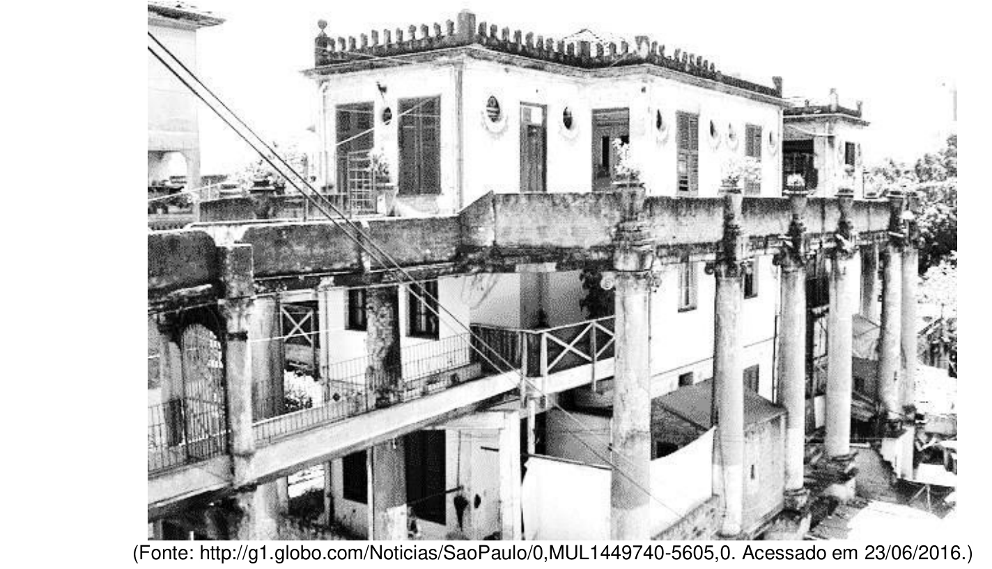 Fotografia em preto e branco de um casarão histórico em estado de degradação na Vila Itororó, com colunatas de sustentação, passarelas improvisadas e roupas estendidas.