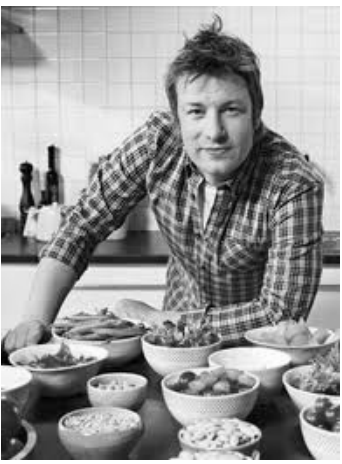 Fotografia em preto e branco do chef James Oliver, de camisa xadrez, debruçado sobre uma bancada repleta de tigelas com alimentos frescos.