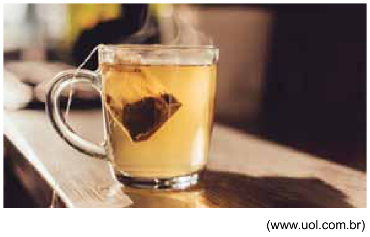 Fotografia de uma caneca de vidro transparente contendo chá e um sachê de chá mergulhado, com a indicação da fonte (www.uol.com.br) no canto inferior direito.
