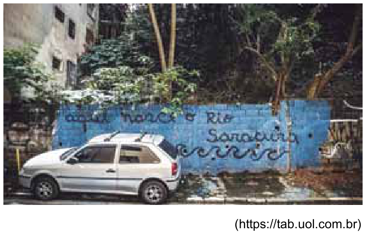 Fotografia urbana mostrando um muro azul com a frase grafitada "aqui nasce o Rio Saracura" e desenhos de ondas abaixo. À frente do muro, vê-se um carro branco estacionado em uma vaga e, atrás e aos lados do muro, árvores e construções.