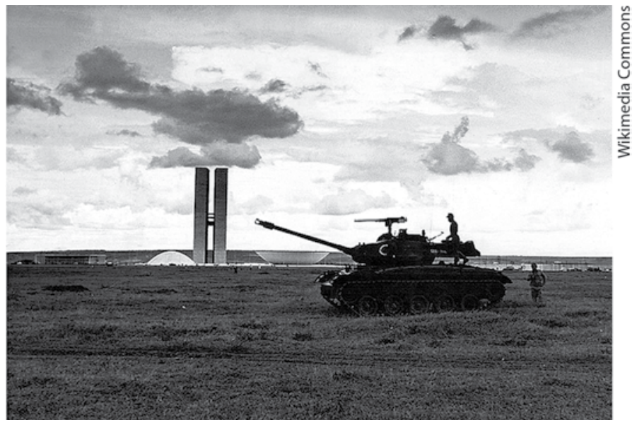 Fotografia em preto e branco de 1964 mostrando um tanque de guerra militar em um campo aberto tendo ao fundo o edifício do Congresso Nacional em Brasília.