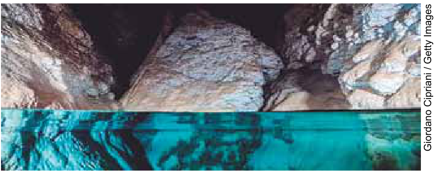 Fotografia do interior de uma formação rochosa subterrânea com água cristalina azulada na parte inferior.