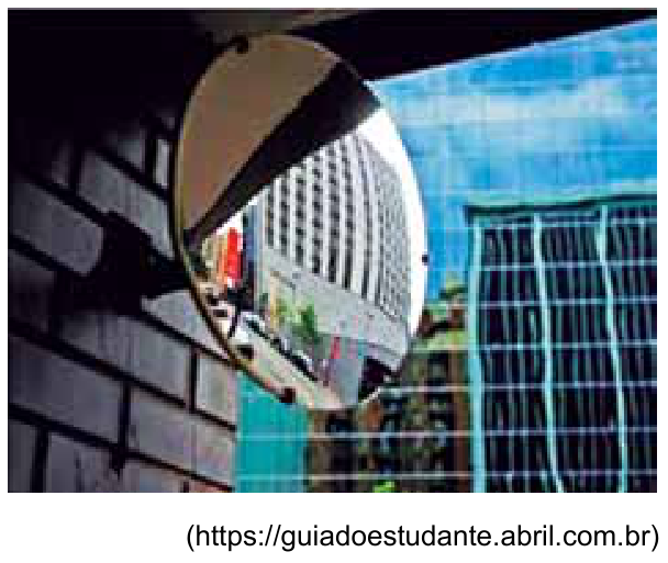 Espelho convexo redondo fixado em parede de tijolos claros refletindo edifícios e a rua