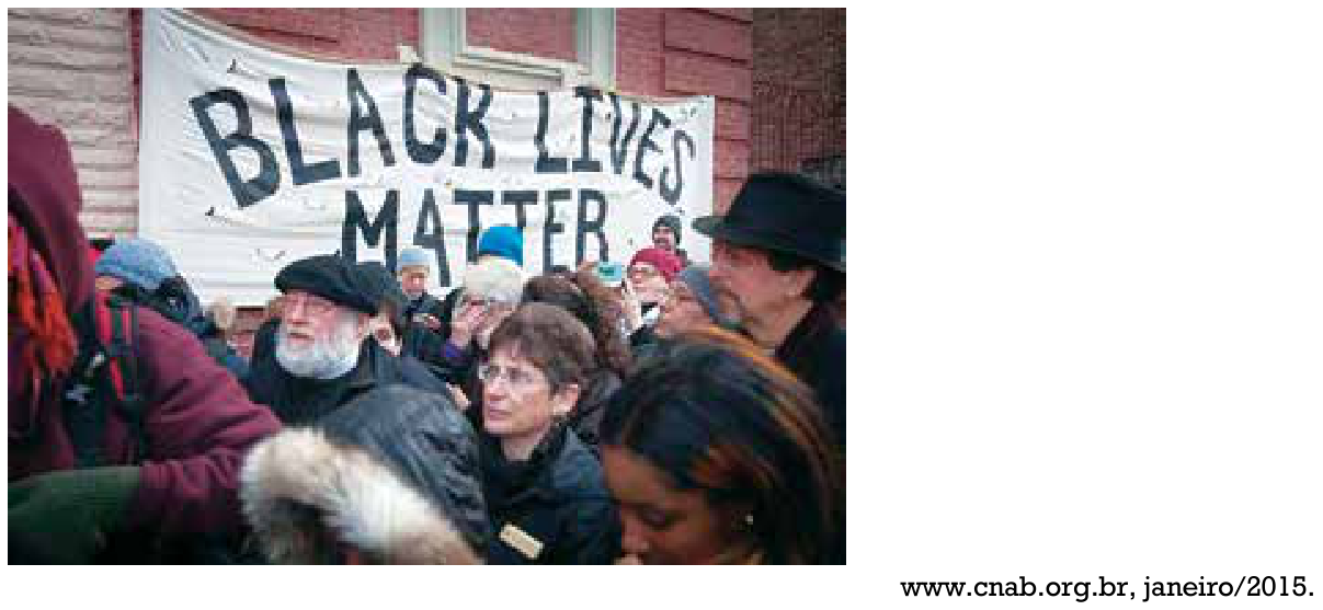 Multidão reunida em manifestação com uma faixa ao fundo na qual está escrito "BLACK LIVES MATTER"