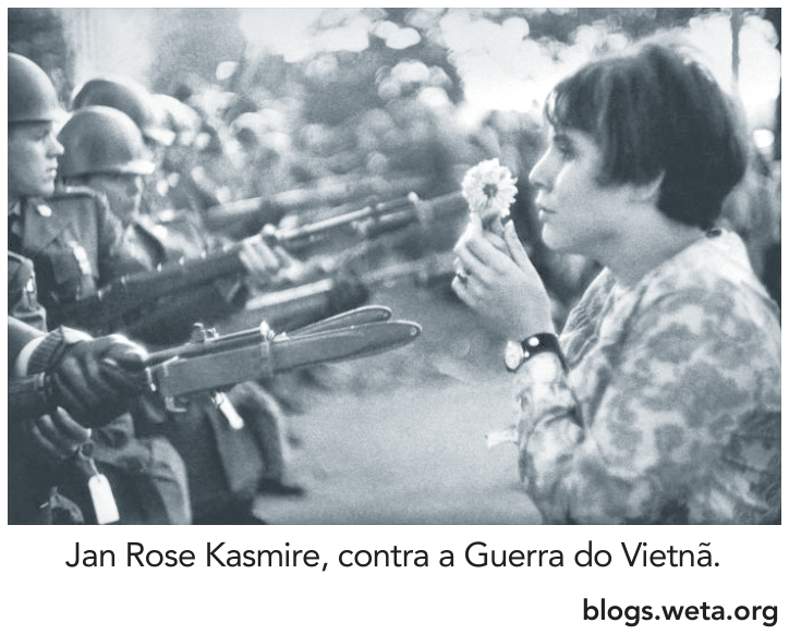 Jan Rose Kasmire segurando uma flor em frente a soldados armados com baionetas.