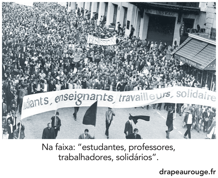 Multidão em passeata pelas ruas de Paris carregando faixa e bandeiras.