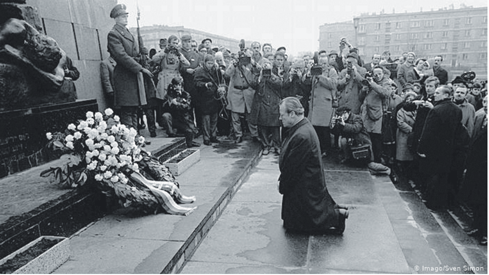 Willy Brandt ajoelhado diante do Memorial aos Heróis do Gueto de Varsóvia, observado por soldados, fotógrafos e jornalistas.