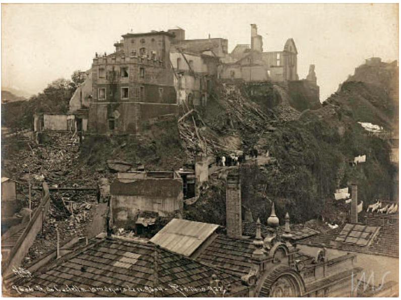 Fotografia da demolição do Morro do Castelo, mostrando encosta com escombros, ruínas de construções e telhados em primeiro plano
