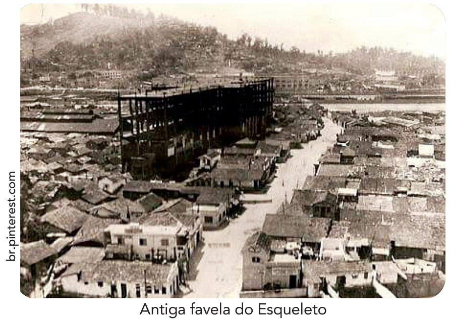 F1 Fotografia da antiga favela do Esqueleto, mostrando uma grande estrutura de concreto inacabada cercada por inúmeras habitações populares.