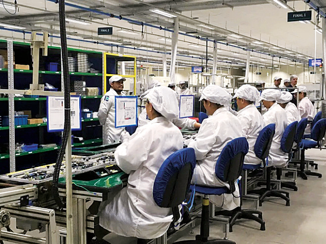 F2 Trabalhadores uniformizados sentados em fileira executam tarefas manuais em uma esteira de produção fabril.