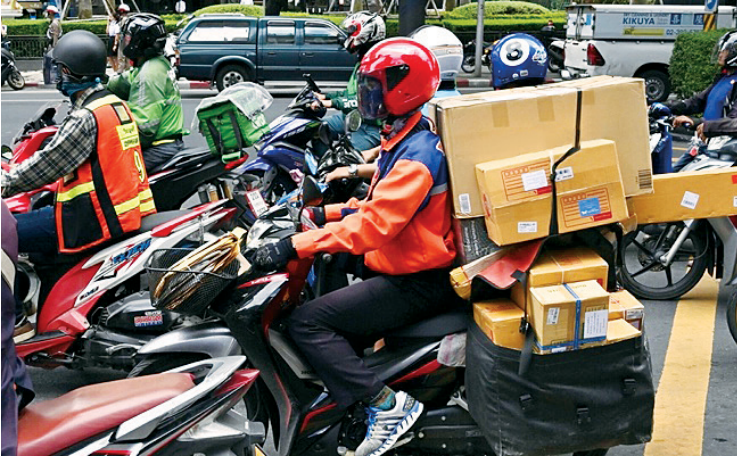 F3 Entregador em uma motocicleta carregada com caixas e pacotes de encomendas no trânsito urbano.
