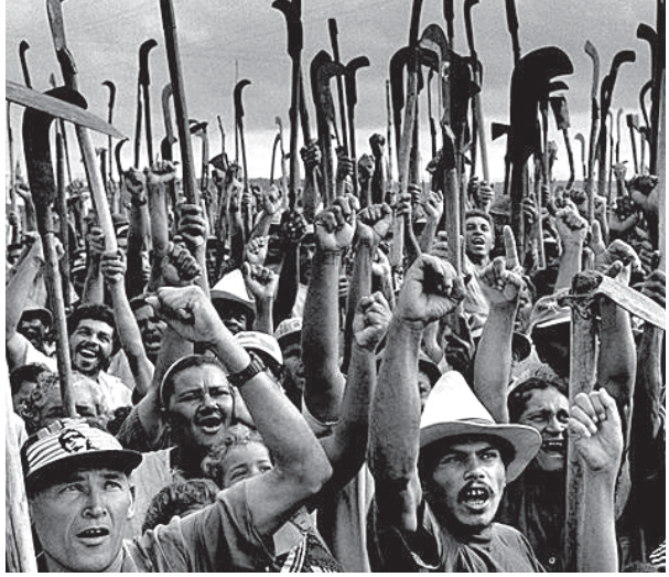 Fotografia em preto e branco de Sebastião Salgado retratando uma multidão de trabalhadores rurais em manifestação coletiva, erguendo foices e punhos cerrados.