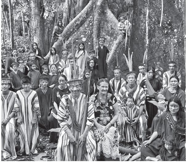 Fotografia em preto e branco de Sebastião Salgado com um retrato posado de um grupo numeroso de indígenas pertencentes a uma mesma comunidade na floresta amazônica, sentados e de pé diante de uma grande árvore.