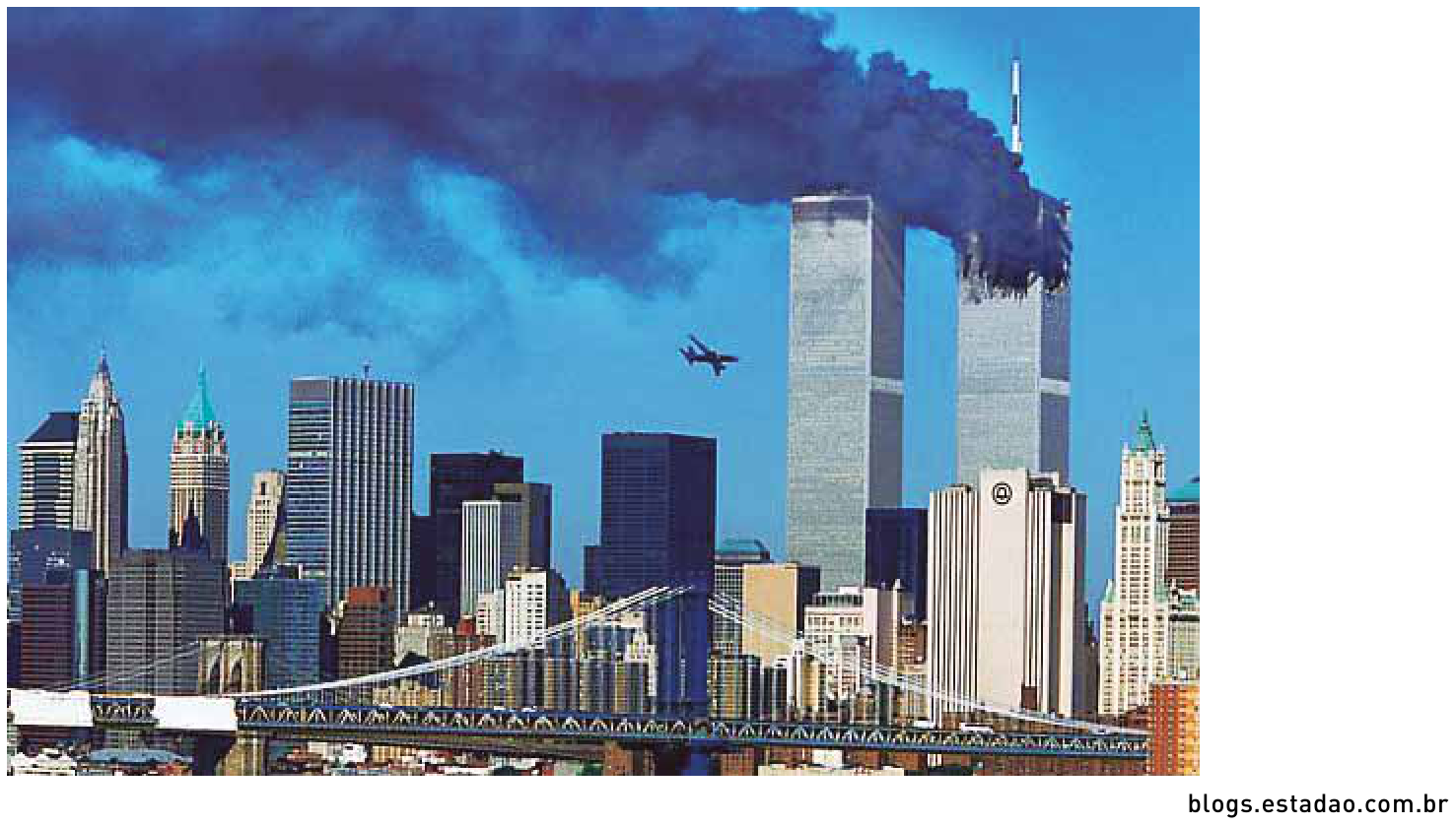 Fotografia da silhueta urbana de Nova York durante os atentados de 11 de setembro de 2001, com as torres gêmeas do World Trade Center em chamas emitindo fumaça preta e um avião comercial se aproximando da segunda torre.