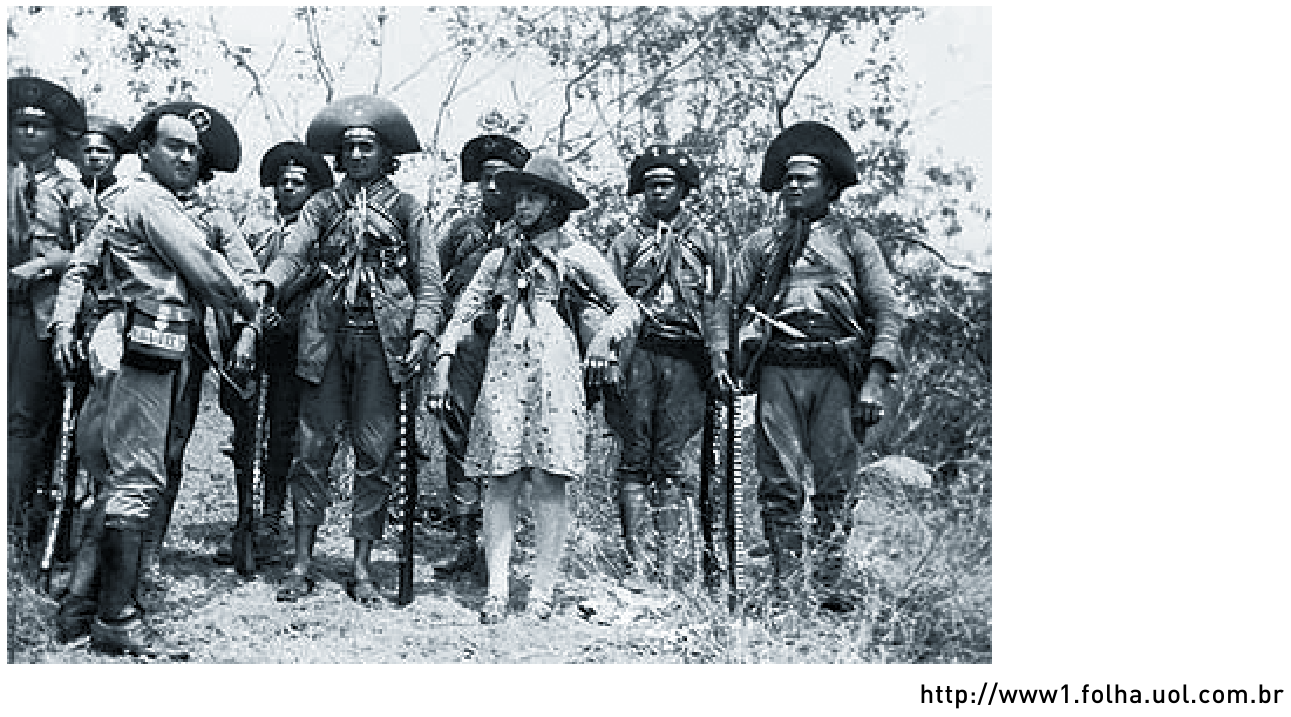 F1 Fotografia histórica em preto e branco do grupo de cangaceiros armados, com destaque para Lampião e Maria Bonita ao centro.