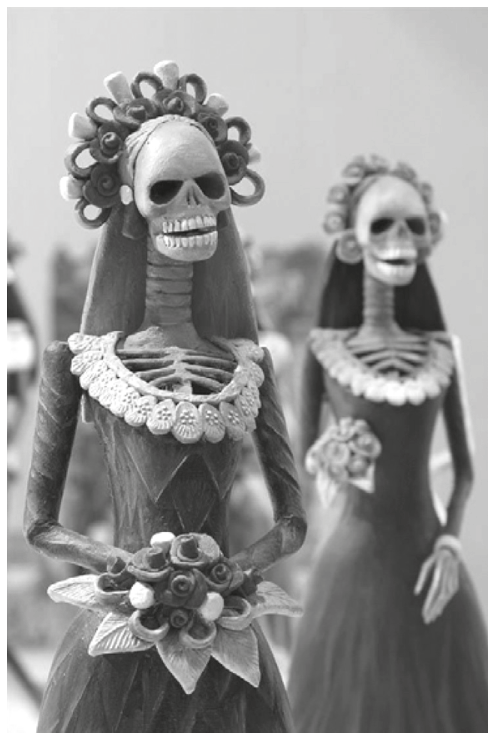 Duas esculturas mexicanas representando esqueletos vestidos com trajes e arranjos florais típicos do Dia dos Mortos