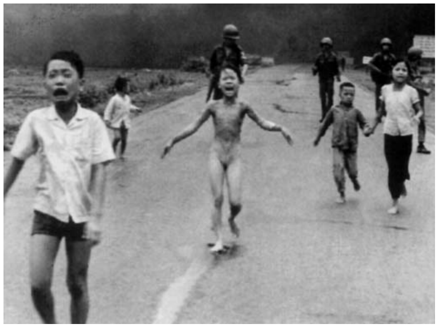 Fotografia histórica em preto e branco mostrando crianças vietnamitas correndo em desespero por uma estrada, chorando e gritando, com soldados armados ao fundo; ao centro, a menina Kim Phúc corre nua após ter suas roupas queimadas por um ataque de napalm.