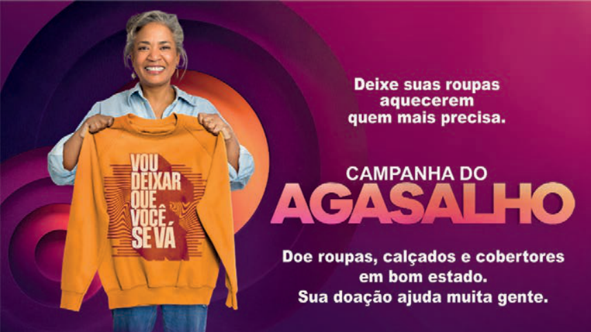 F1 Cartaz da Campanha do Agasalho, com uma mulher segurando um moletom onde está escrito "VOU DEIXAR QUE VOCÊ SE VÁ". Ao lado, o texto: "Deixe suas roupas aquecerem quem mais precisa. CAMPANHA DO AGASALHO. Doe roupas, calçados e cobertores em bom estado. Sua doação ajuda muita gente."