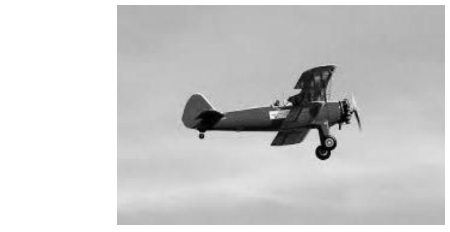 Fotografia em preto e branco de um avião biplano voando horizontalmente da esquerda para a direita