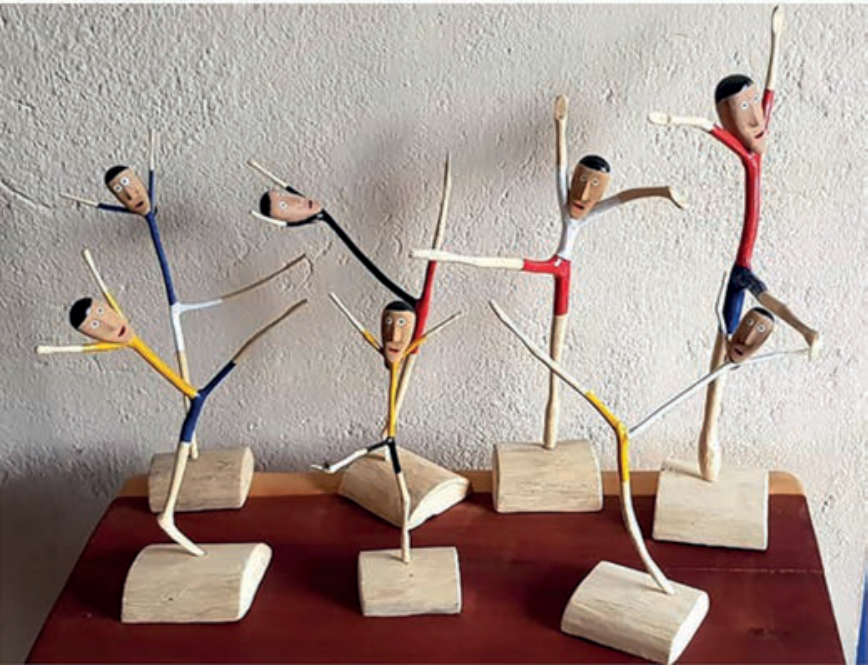 Esculturas de bailarinos feitos com gravetos de madeira entalhados e pintados, em poses de dança, fixados sobre pequenas bases retangulares de madeira.