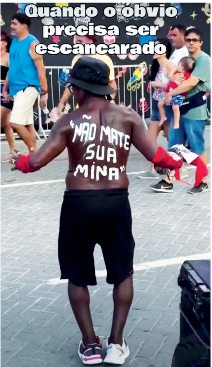 Fotografia de um homem negro visto de costas na rua durante o carnaval, vestindo bermuda preta e chapéu preto, sem camisa, com a frase "NÃO MATE SUA MINA" pintada em branco nas costas. No topo da imagem, há a legenda: "Quando o óbvio precisa ser escancarado".