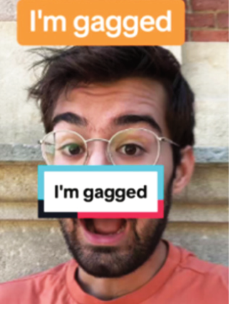 F1 Print de vídeo do linguista Adam Aleksic com expressão de espanto, de boca aberta e usando óculos; sobre sua boca há uma tarja com os dizeres "I'm gagged" e, no topo da imagem, uma etiqueta laranja com a mesma frase.