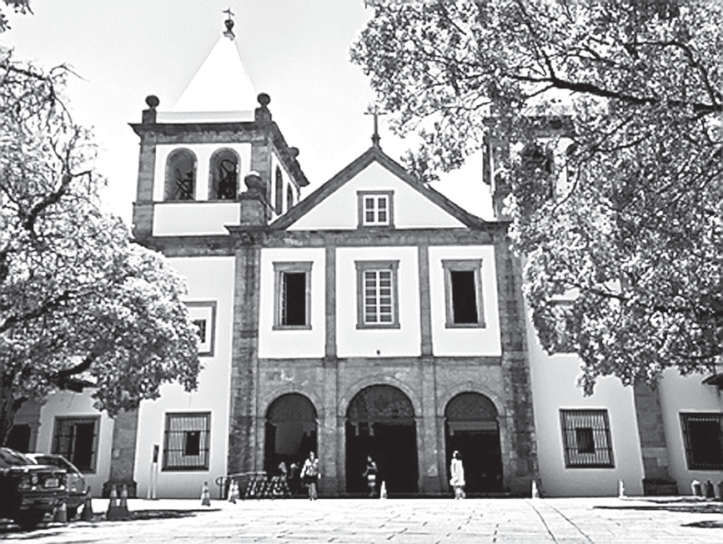 F1 Fachada da igreja e mosteiro colonial em tons de branco e pedra, com torres sineiras e árvores aos lados.