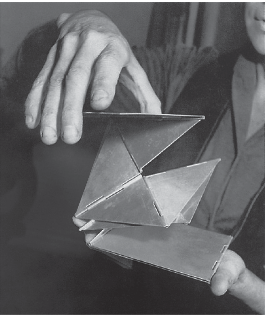 Fotografia em preto e branco que mostra mãos manipulando a escultura geométrica articulada formada por placas de metal dobradas e unidas por dobradiças, intitulada Bicho de bolso, de Lygia Clark.
