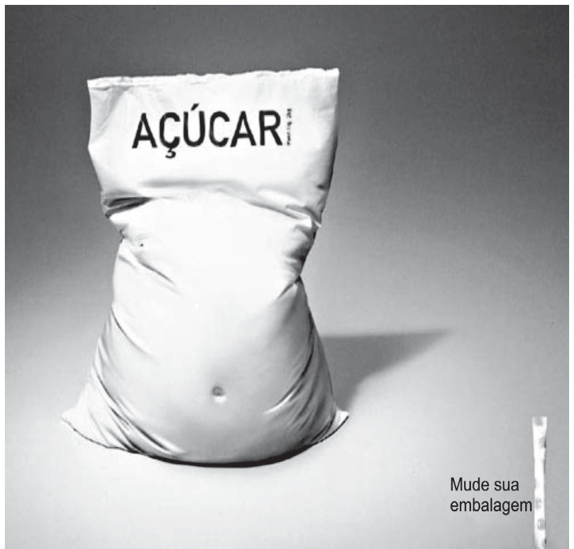 F1 Anúncio publicitário mostrando um saco de açúcar com a palavra "AÇÚCAR" na parte superior, moldado no formato de um abdômen proeminente com umbigo, sugerindo um corpo humano com sobrepeso. No canto inferior direito, aparece um sachê estreito e longo de adoçante ao lado da frase "Mude sua embalagem".