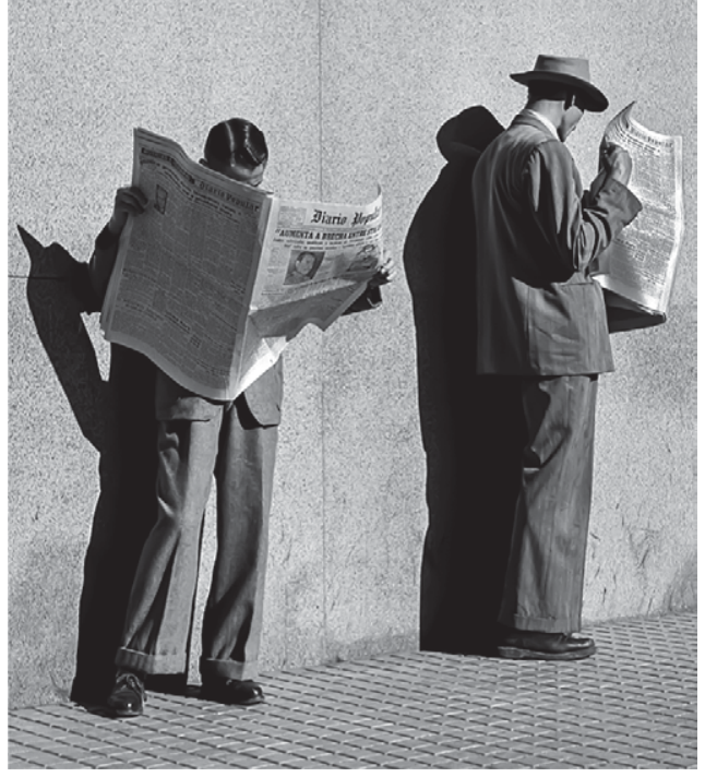 Fotografia em preto e branco de dois homens vestindo trajes formais, parados em uma calçada de lajotas limpas junto a uma parede clara. Sob sol forte que projeta sombras nítidas, ambos leem exemplares abertos do jornal Diário Popular. O homem à esquerda está de frente com o jornal cobrindo a parte superior de seu rosto; o da direita está de perfil e usa chapéu.