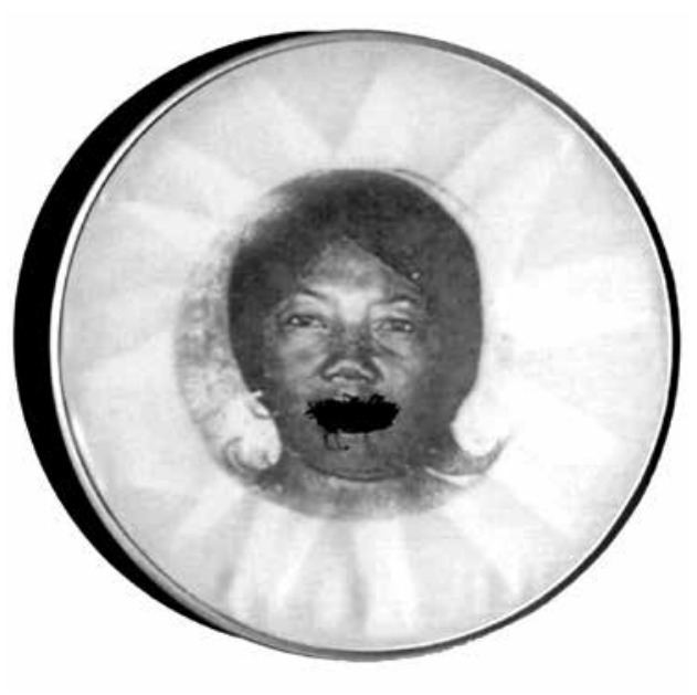 Fotografia em preto e branco de um bastidor circular de madeira para bordado, contendo a imagem impressa do rosto de uma mulher negra com a boca costurada por linhas pretas entrecruzadas.