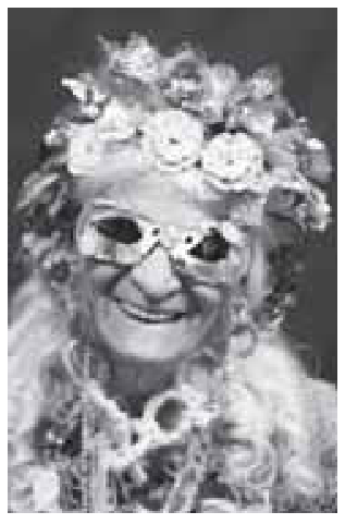 Fotografia em preto e branco da artista Efigênia Ramos Rolim sorrindo, usando óculos decorados e adereços na cabeça e no corpo feitos a partir de materiais recicláveis.