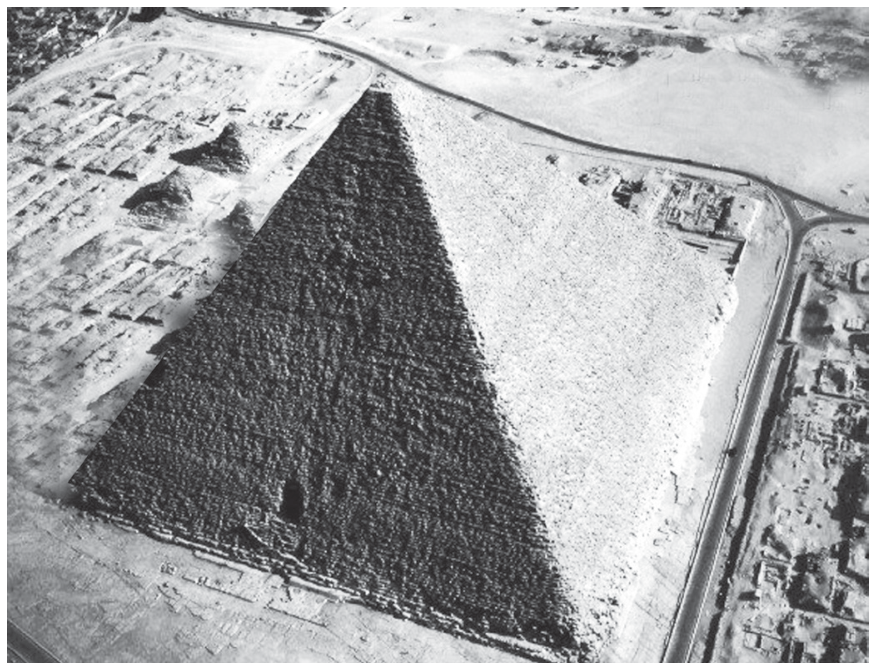 Fotografia aérea em preto e branco da Pirâmide de Quéops, destacando duas de suas faces triangulares e a paisagem ao redor.