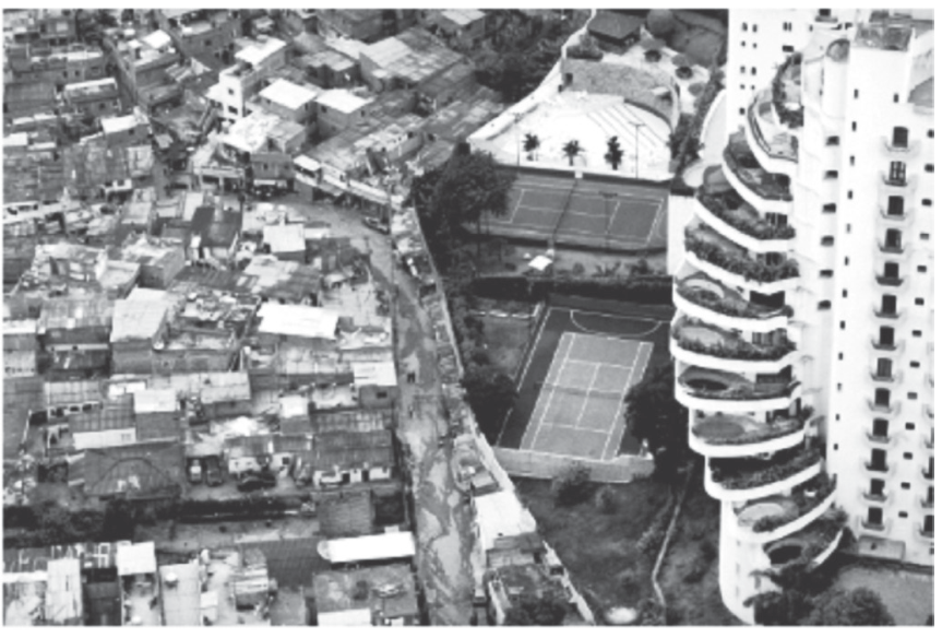 Fotografia aérea mostrando a disparidade social e urbana no limite entre a comunidade de Paraisópolis (à esquerda), com habitações populares aglomeradas e precárias, e o bairro nobre do Morumbi em São Paulo (à direita), com um edifício de luxo com piscinas nas varandas e quadras esportivas privativas.