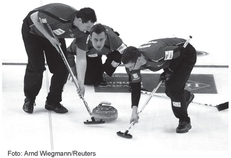 F1 Jogadores de curling em uma pista de gelo; dois deles utilizam vassouras para varrer a superfície logo à frente da pedra de granito em movimento, enquanto o terceiro observa agachado.