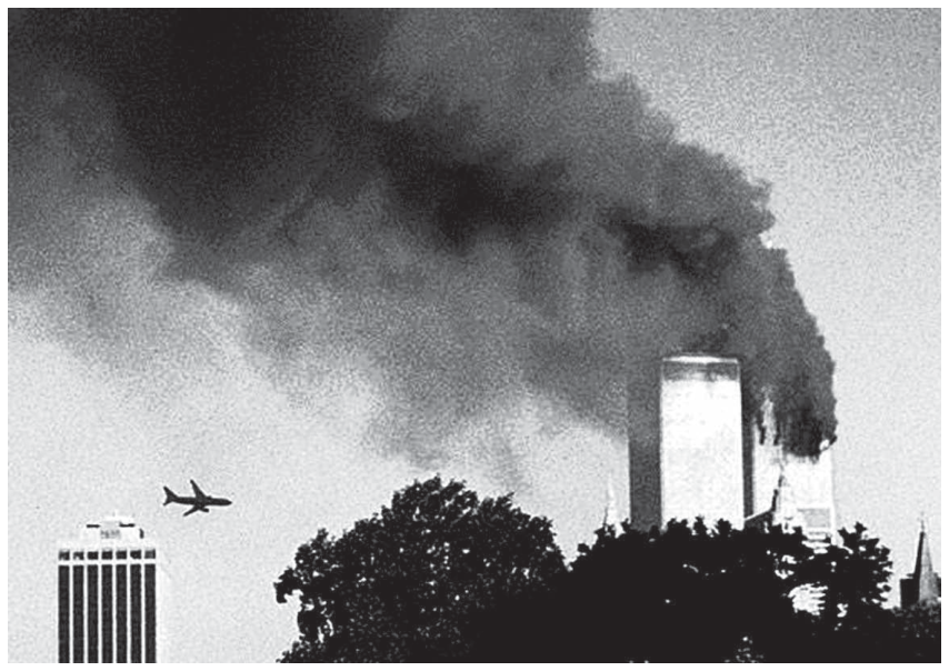Fotografia em preto e branco do atentado de 11 de setembro de 2001 em Nova York, mostrando as torres do World Trade Center cobertas por densa fumaça escura, com um avião comercial voando em direção a elas.