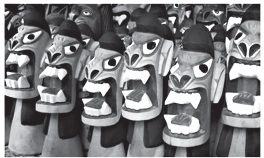Fotografia de várias esculturas de carrancas de madeira enfileiradas, esculpidas com expressões ferozes, olhos esbugalhados e bocas abertas exibindo dentes.