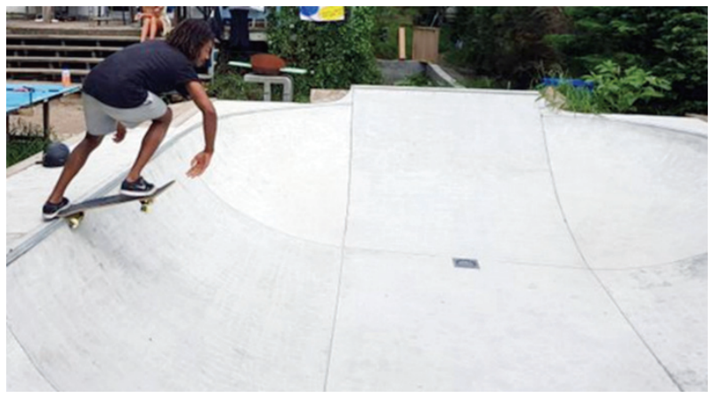 Fotografia de um skatista posicionado na borda superior de uma pista de skate do tipo bowl (formato de bacia) de concreto.