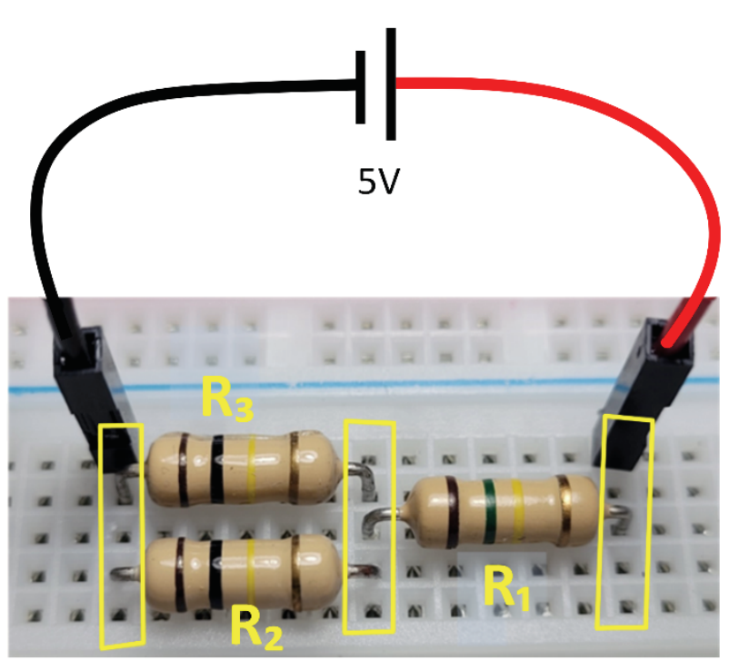 F1 Fotografia de um circuito montado em uma protoboard com resistores R1, R2 e R3. Os resistores R2 e R3 estão dispostos em paralelo entre dois nós verticais delimitados por retângulos amarelos. O resistor R1 conecta o nó intermediário a um terceiro nó à direita. Cabos preto e vermelho conectam as extremidades do circuito a uma fonte de tensão contínua esquematizada de 5 V.