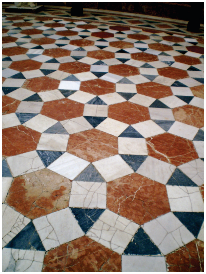Fotografia do piso de um museu em Sevilha composto por ladrilhos poligonais de mármore colorido.